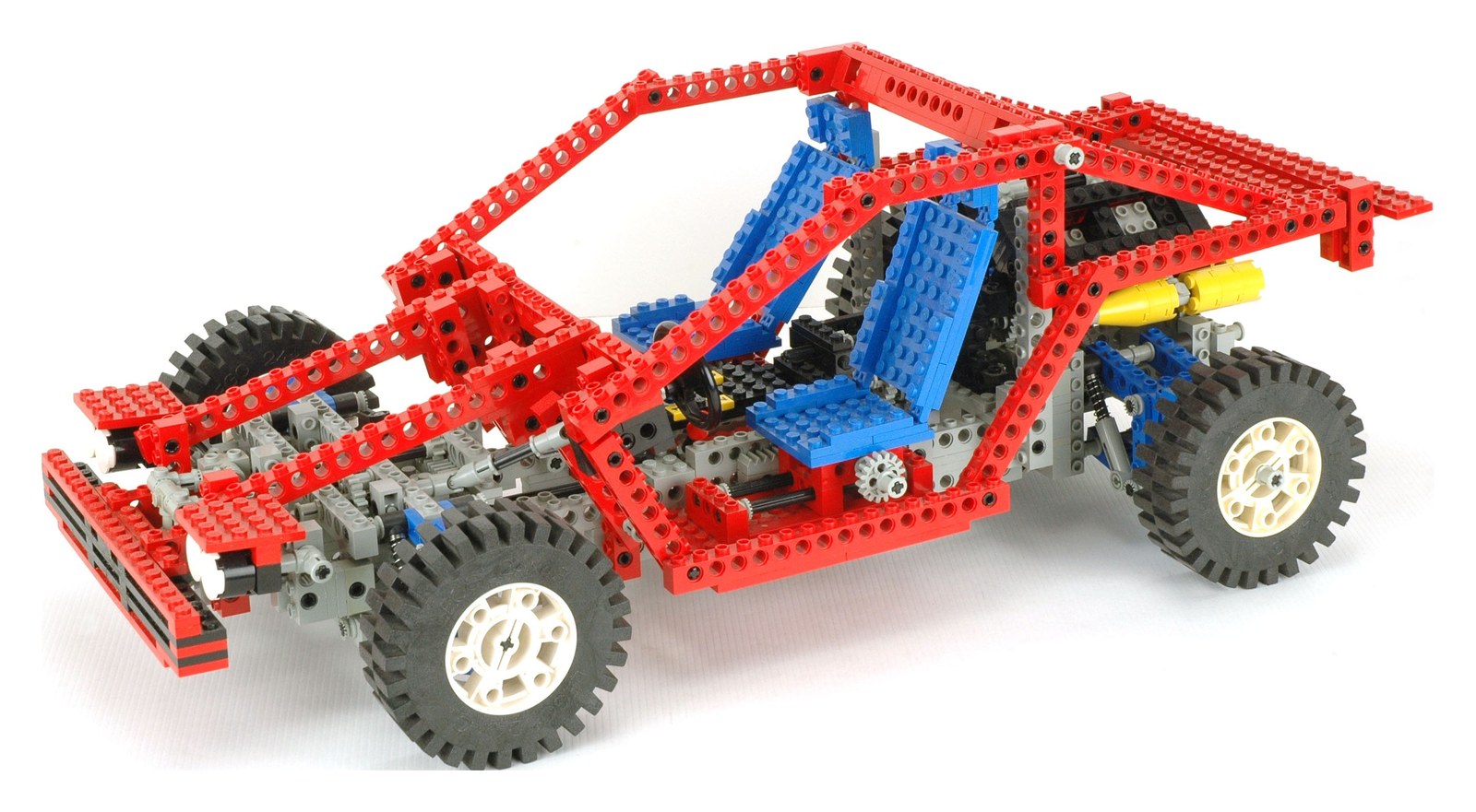 A red LEGO Technic 8865 car with visible mechanical beams, large wheels, and steering and suspension assemblies.